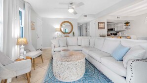 Un salon moderne avec un canapé d’angle blanc, une table basse ronde et un ventilateur de plafond.