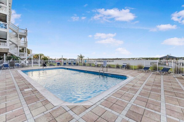 A rectangular pool with a tiled deck, surrounded by a white fence and lounge chairs. - Lagoon Run 113 - Shangri-lala (Gulf Shores)