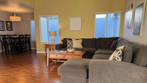 A living room with a sectional sofa, a dining table with chairs, and a lamp. - Spacious Family Home with Fenced Yard (Modesto)