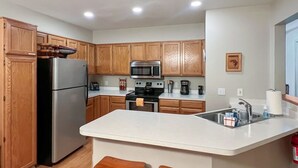 A compact kitchen with wooden cabinets, a stainless steel refrigerator, a microwave, an oven, and a sink. - Convenient Townhome Near Downtown McCall (McCall)