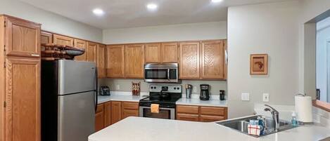 A compact kitchen with wooden cabinets, a stainless steel refrigerator, a microwave, an oven, and a sink.