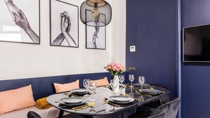 Un coin repas avec une table ronde pour quatre personnes, des chaises noires, un mur d’accent bleu et un téléviseur fixé au mur.