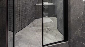 Une douche moderne dotée d’une porte en verre, de murs carrelés et d’un sol en marbre.