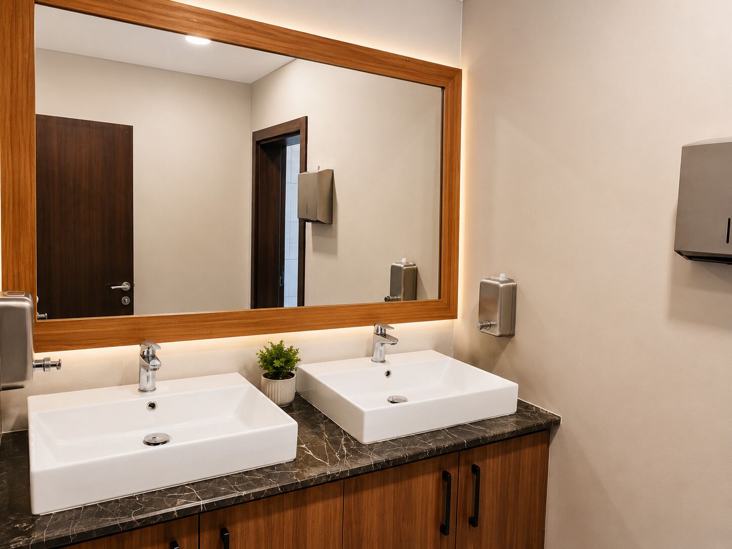 A bathroom with two sinks, a large mirror, a wooden door, and a soap dispenser.