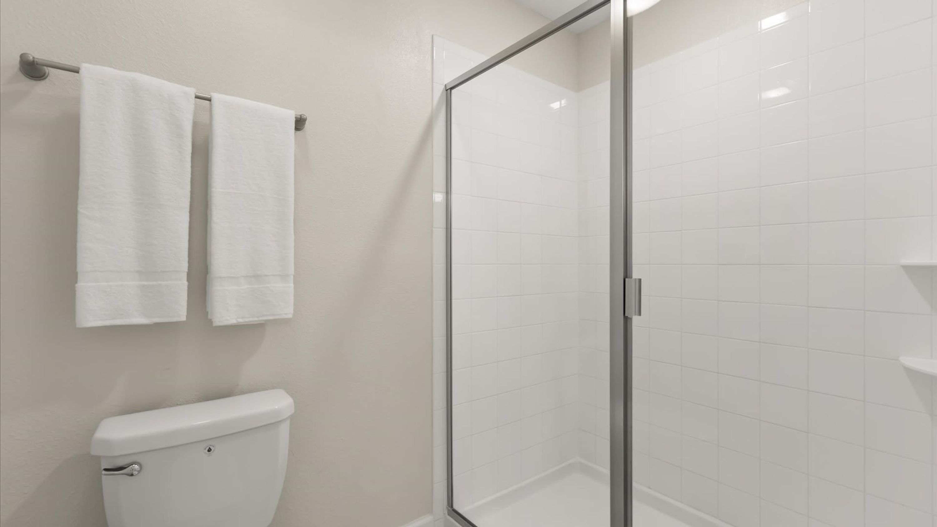 A bathroom with a toilet, two white towels hanging on a rack, and a glass shower enclosure.