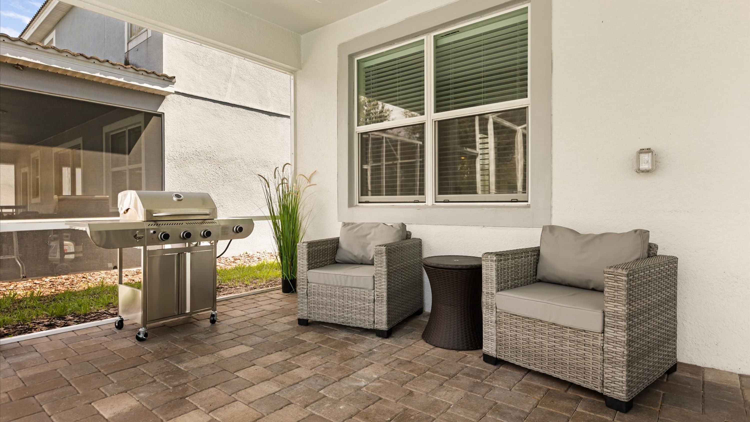 An outdoor patio with a grill, two wicker sofas, and a window with blinds.