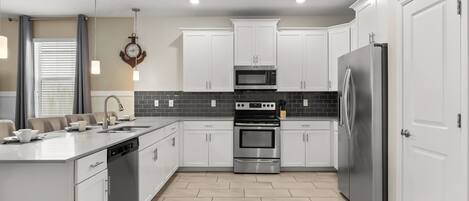 A modern kitchen with white cabinets, a stainless steel refrigerator, a built-in oven, and a microwave.