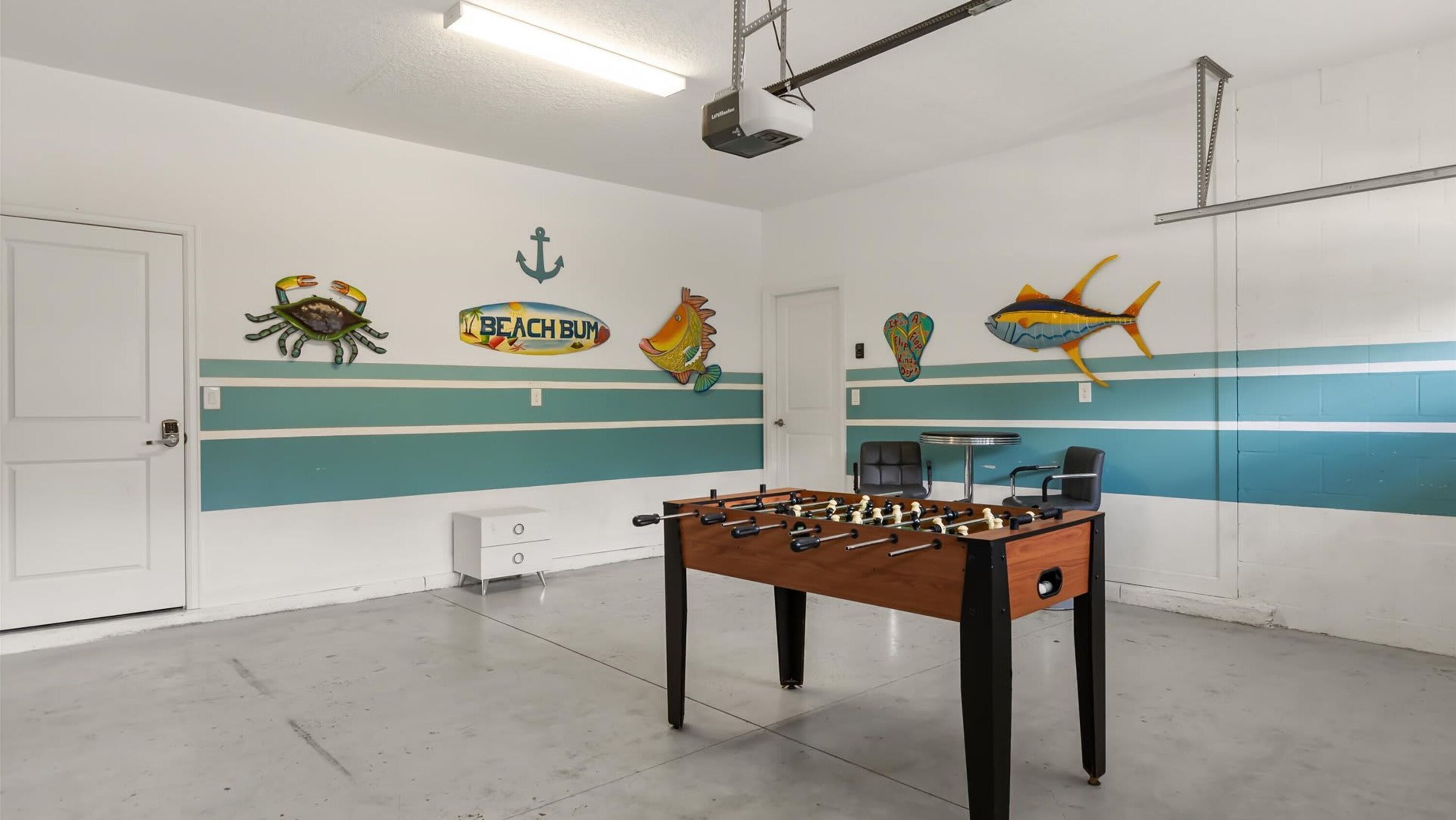 Ein Zimmer mit Fußballtisch, Projektor und Wanddekorationen, darunter Fische und ein Anker.