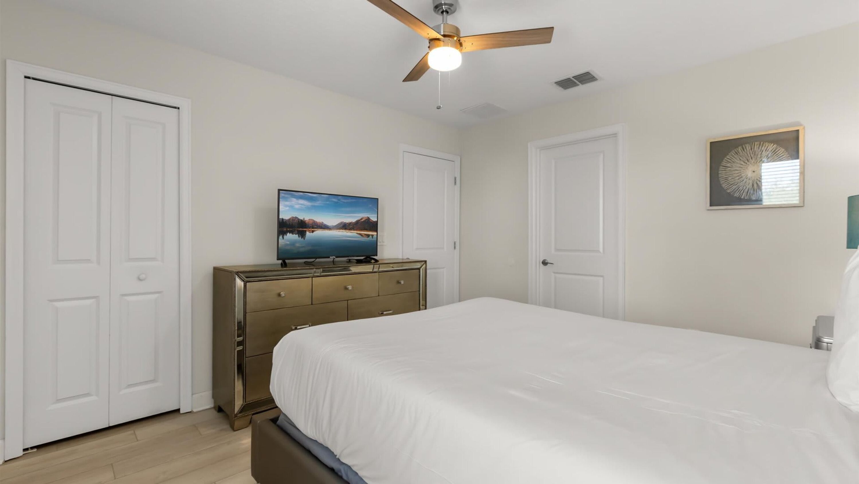 A bedroom with a bed, a dresser, a ceiling fan, and a television on a dresser.