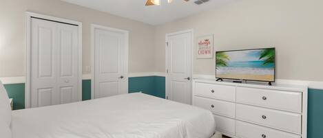 A bedroom with a bed, a dresser, a ceiling fan, and a TV displaying a beach scene.