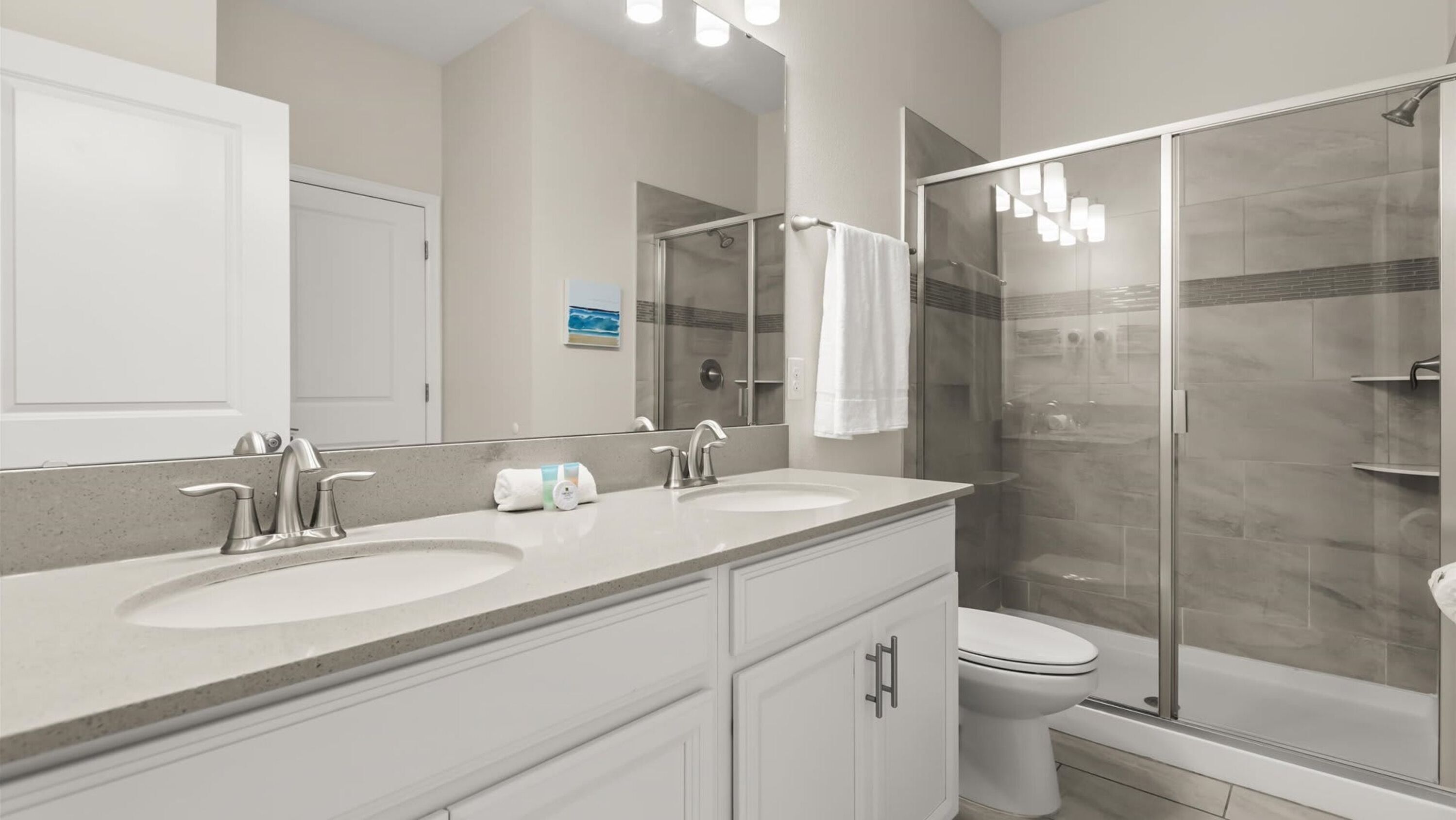 A modern bathroom with two sinks, a shower, and a toilet.