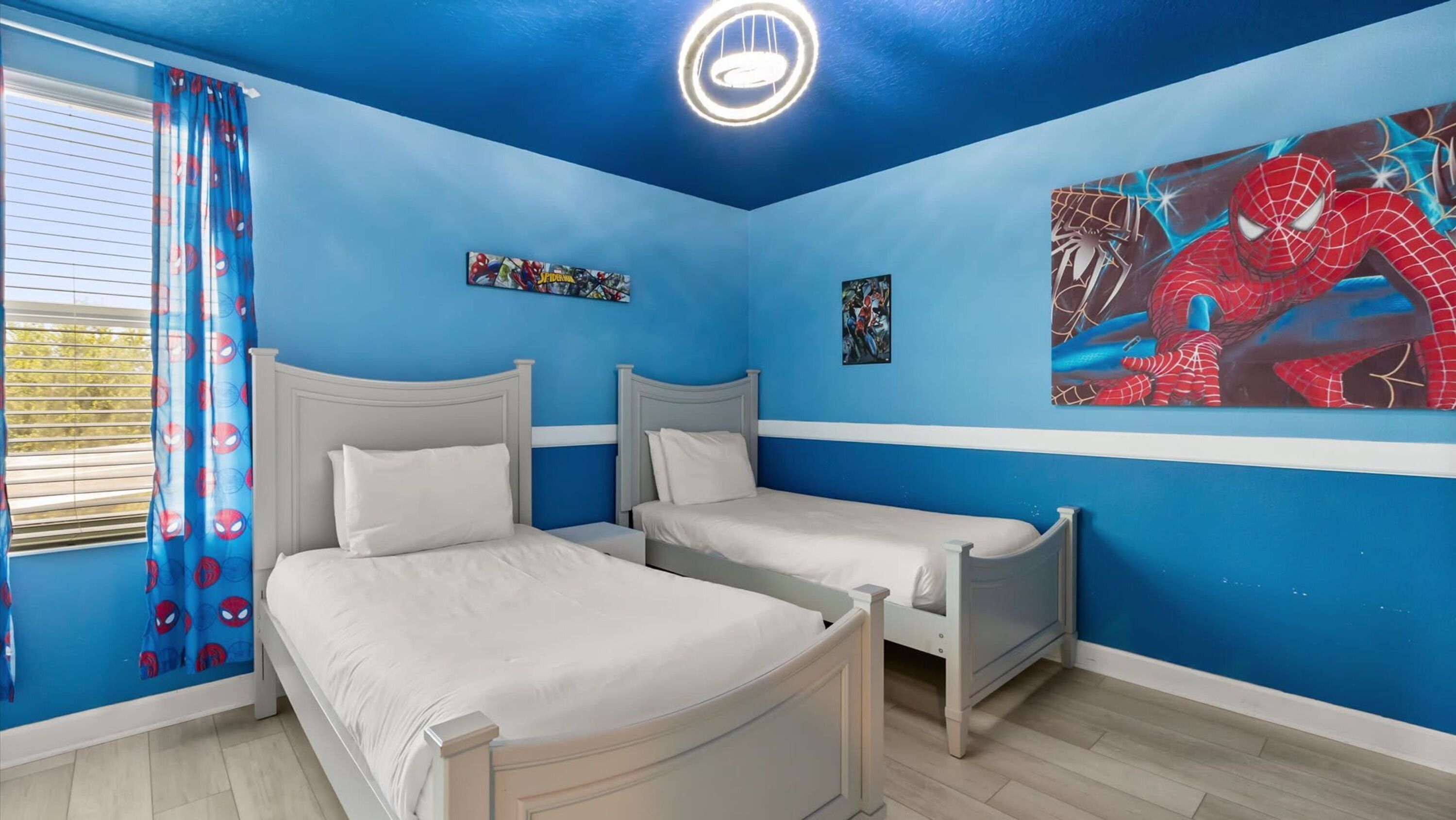 Une chambre avec deux lits, des murs bleus et une décoration sur le thème de Spider-Man.