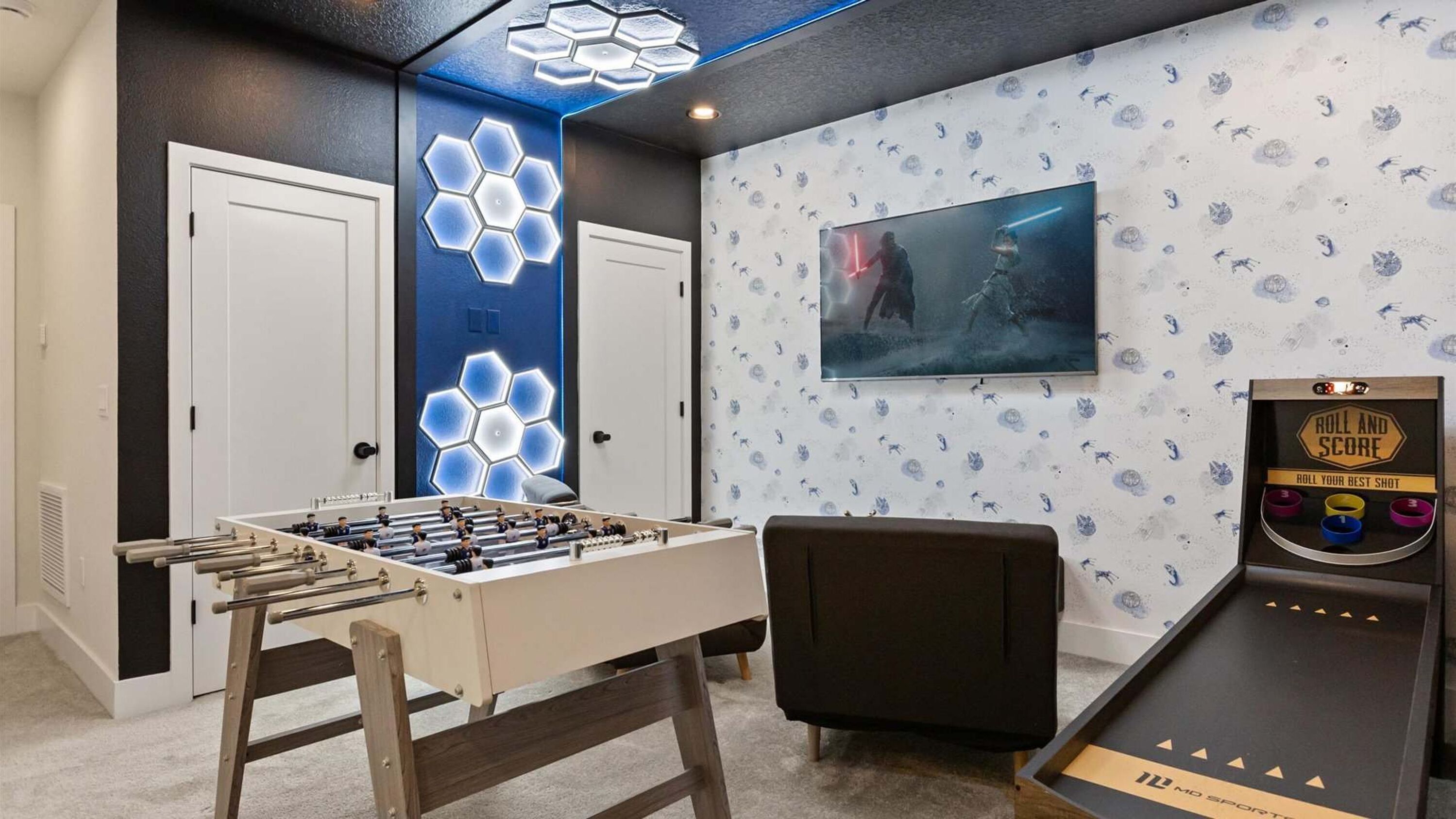 Una habitación con mesa de fútbol de mesa, televisor montado en la pared y una máquina de videojuegos 'Roll and Score'.