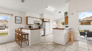 A modern kitchen with white cabinets, a central island with stools, and a dining area with chairs. - Upstay 3BR Family-friendly Stylish Retreat w Patio (Kissimmee)