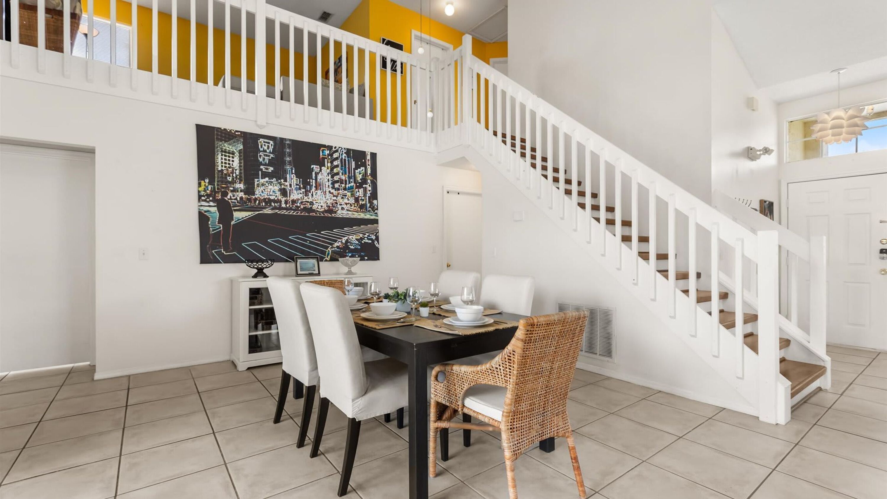A dining area with a black table, white chairs, and a painting of a cityscape.