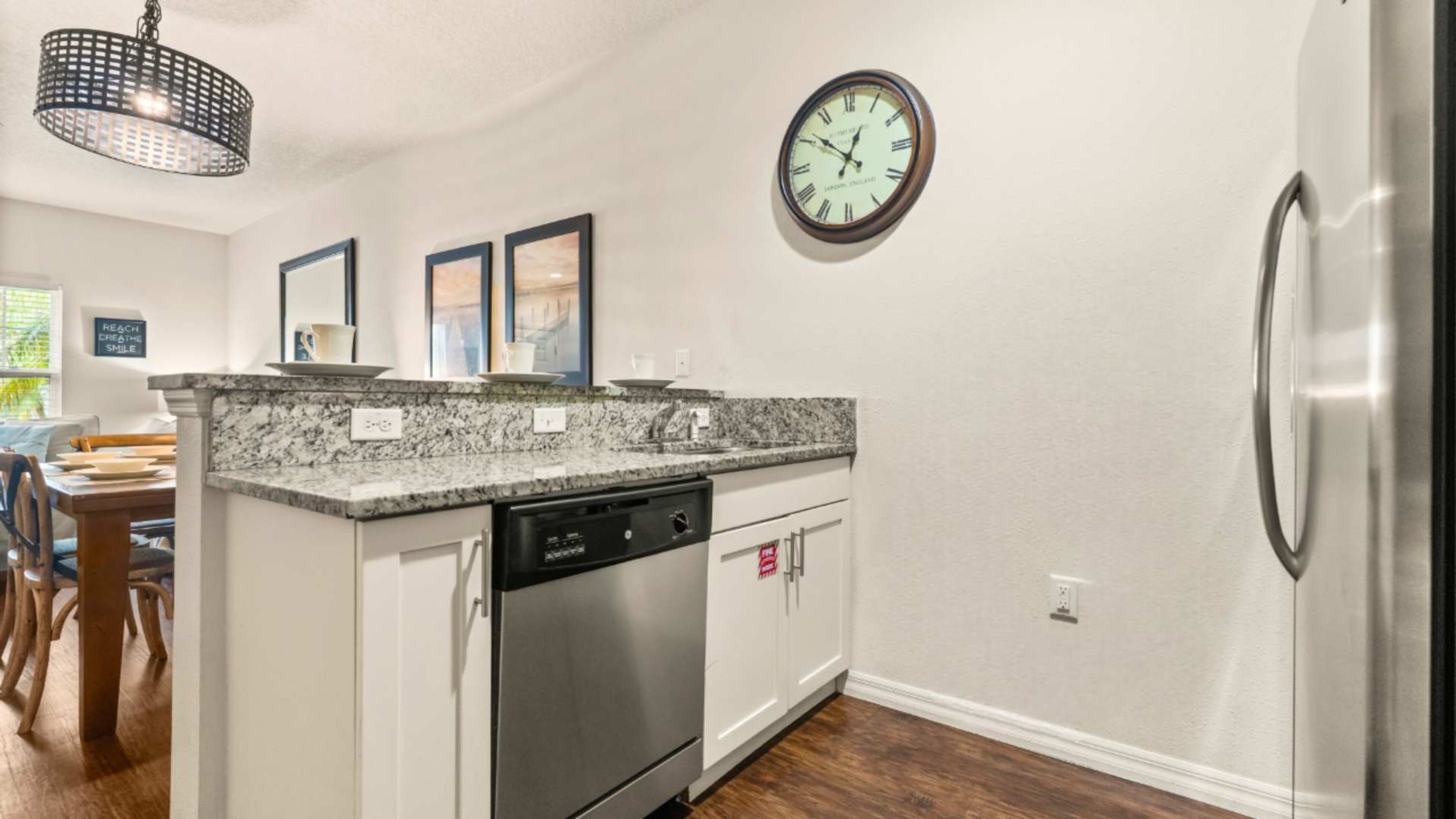 A kitchen with a granite countertop, stainless steel dishwasher, and a wall-mounted clock.