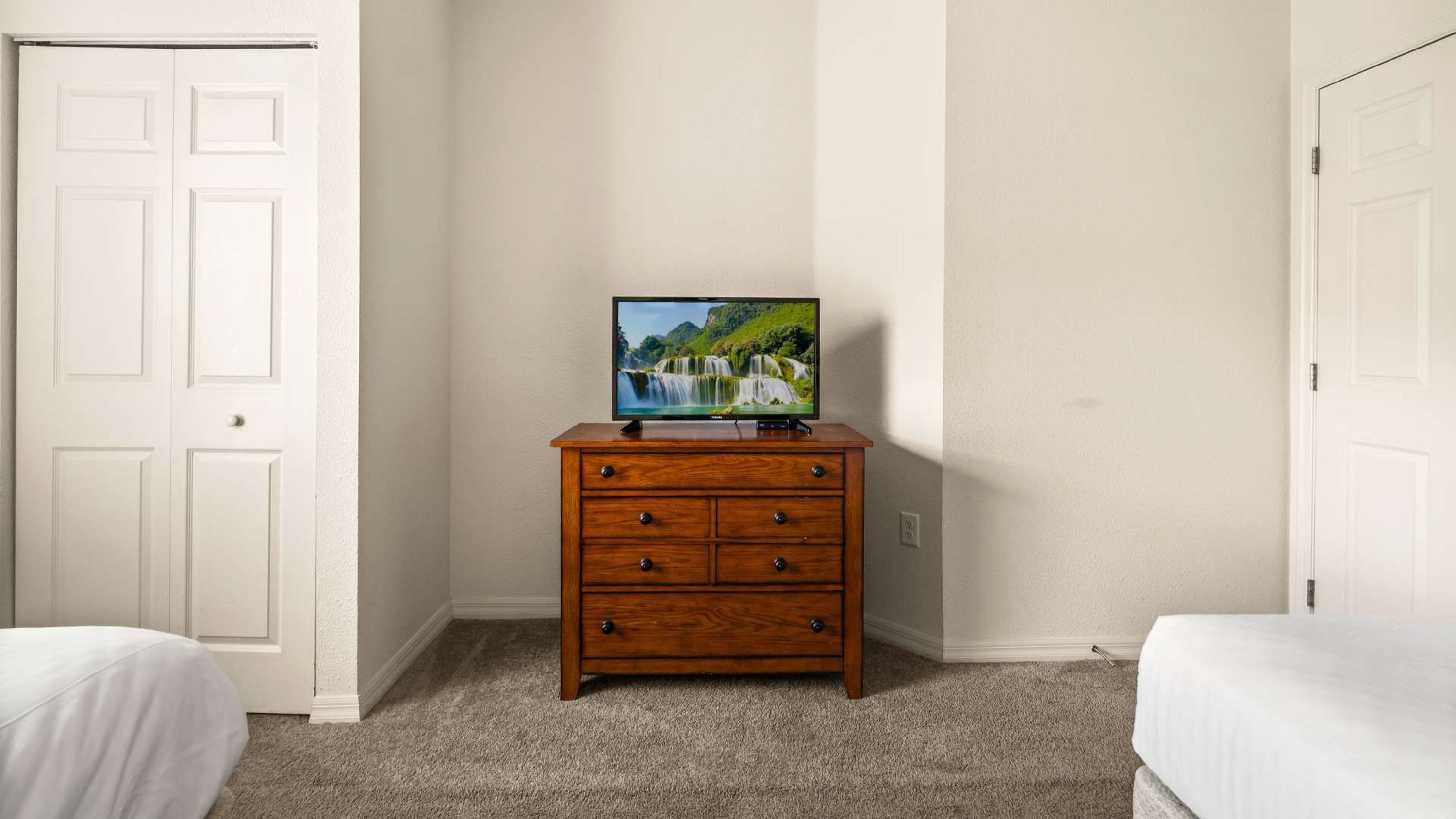 A bedroom with a wooden dresser, a television on top, and two beds.
