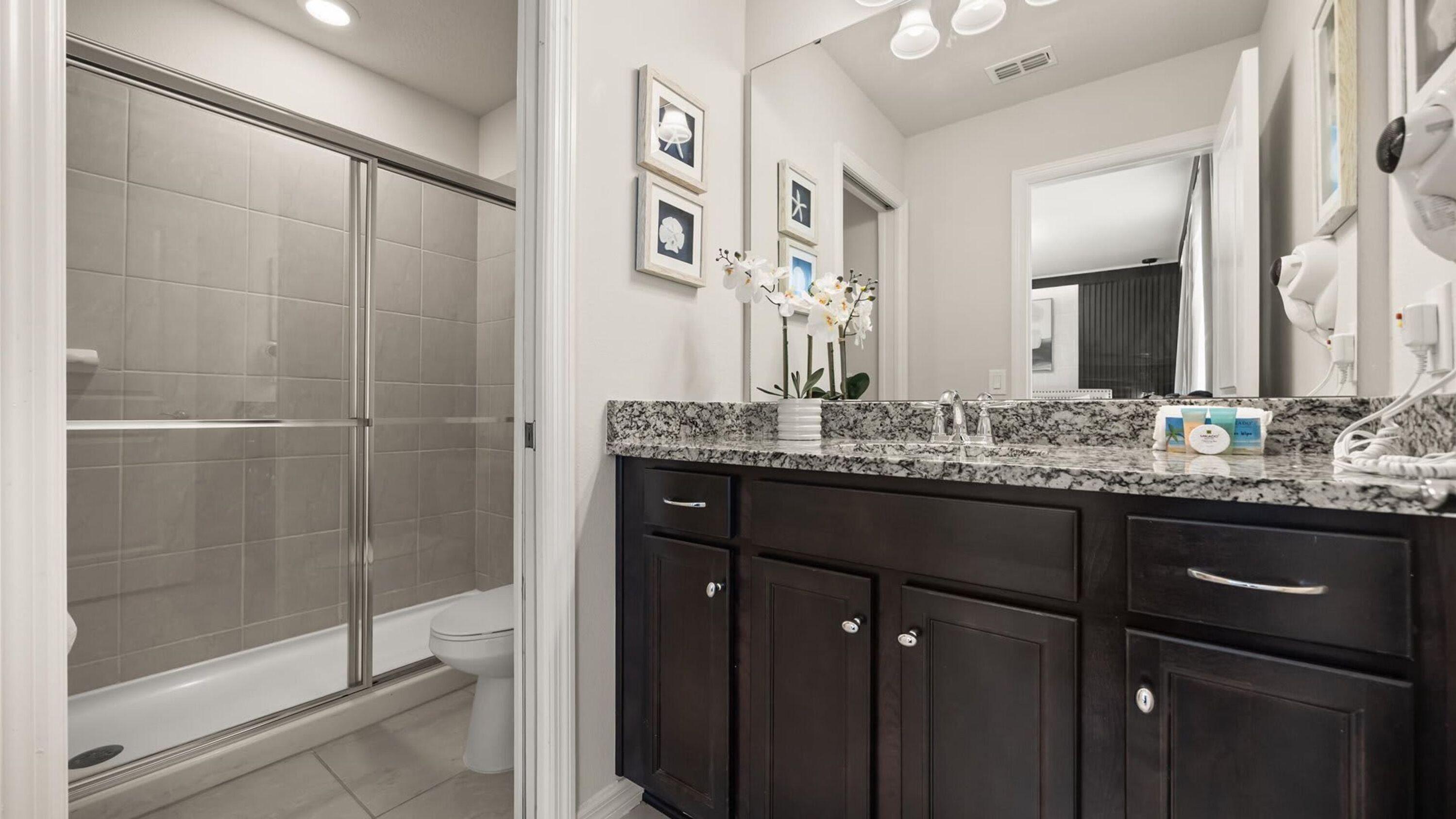 A modern bathroom with a shower, toilet, dark wooden cabinets, a granite countertop, and a large mirror.