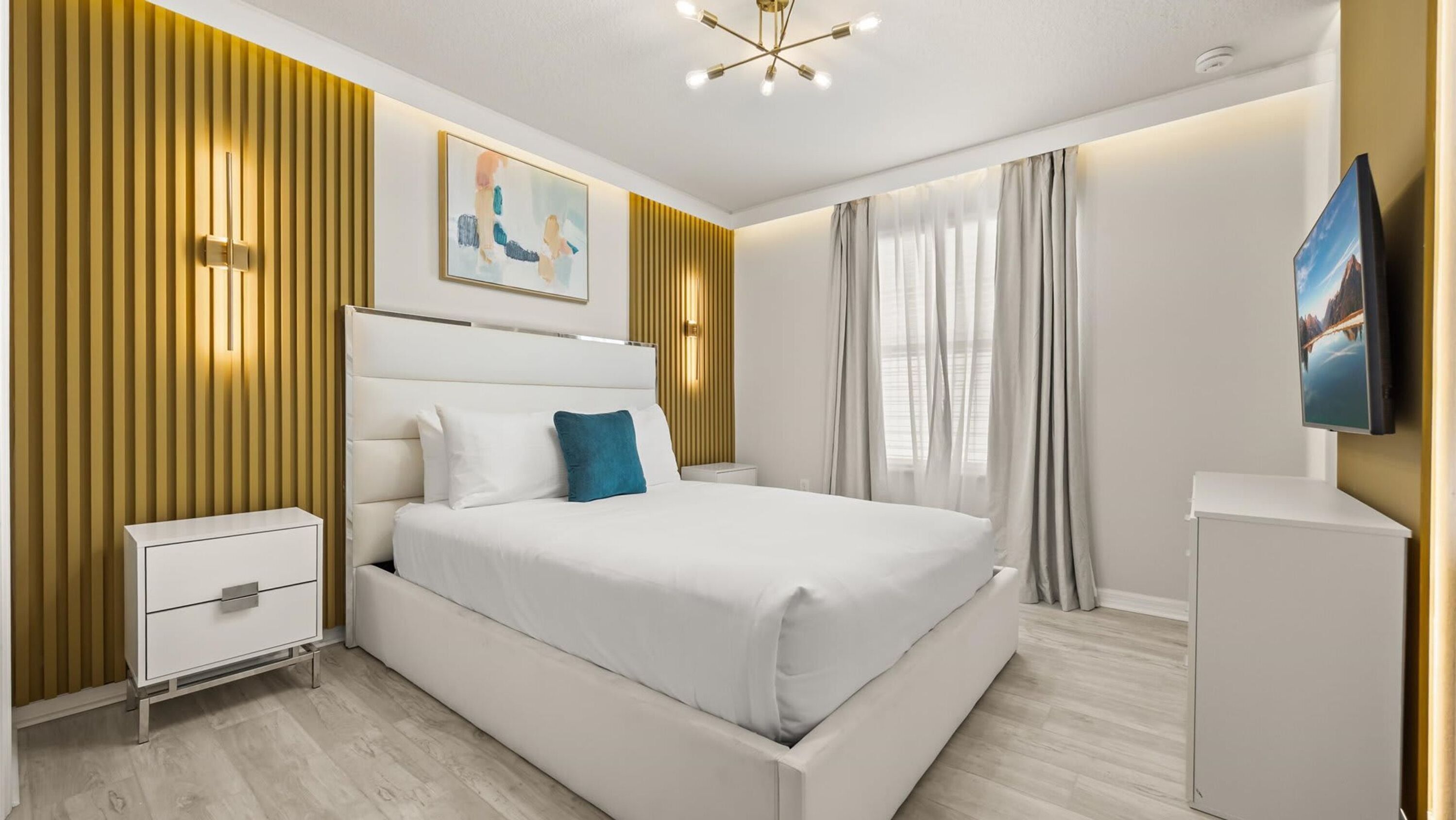 A modern bedroom with a large bed, bedside tables, a mounted TV, and a painting on the wall.