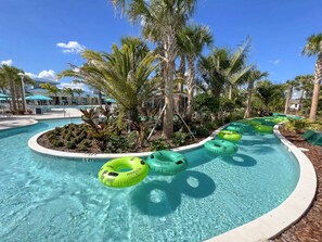 Una piscina con agua cristalina, rodeada de palmeras y un edificio de resort al fondo.