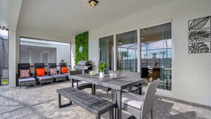 An outdoor patio with a dining table, chairs, and a grill. - Upstay 10br Family Retreat w Pool Hot Tub Games (Clermont)