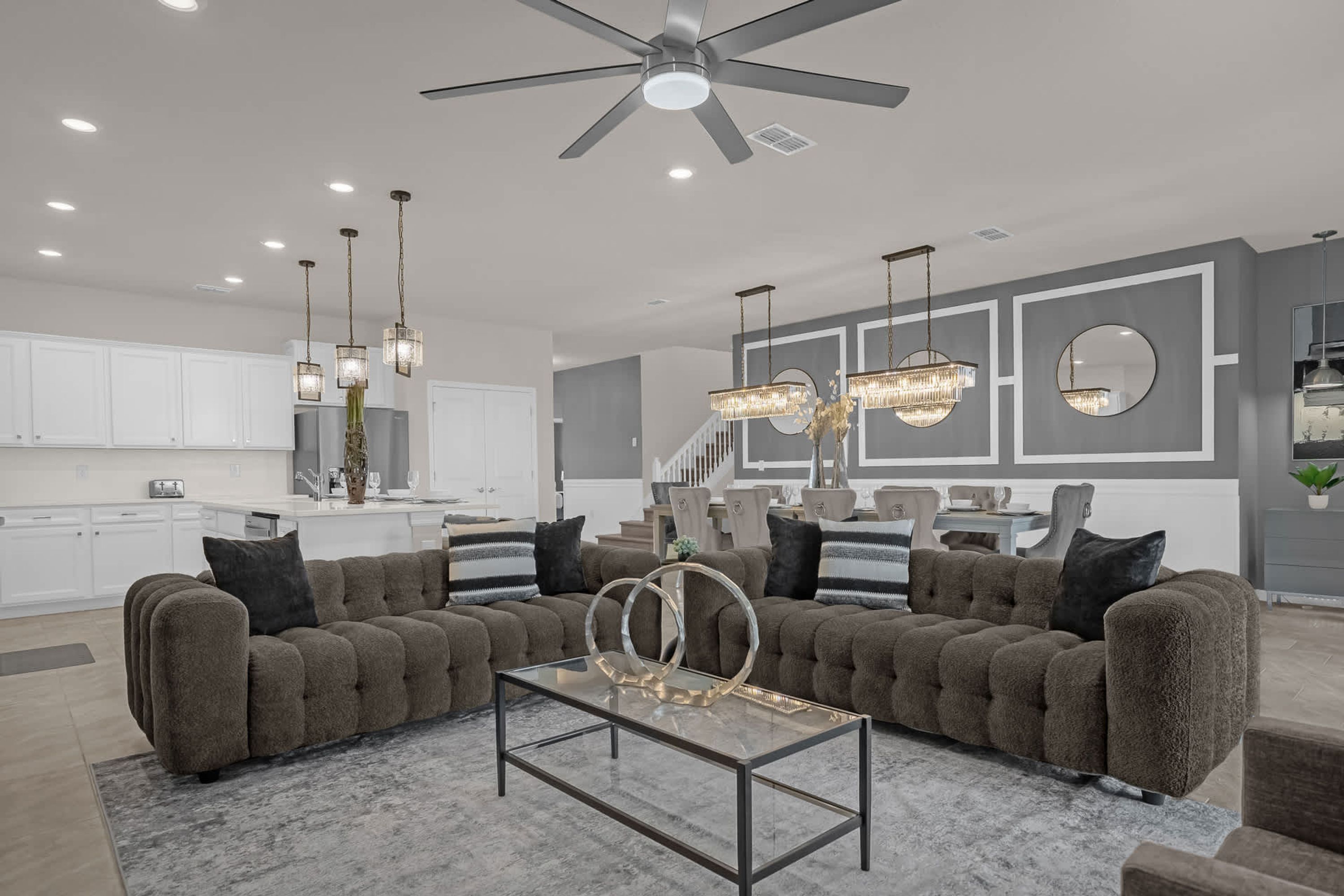 A modern living room with a large sectional sofa, a glass coffee table, and a ceiling fan.