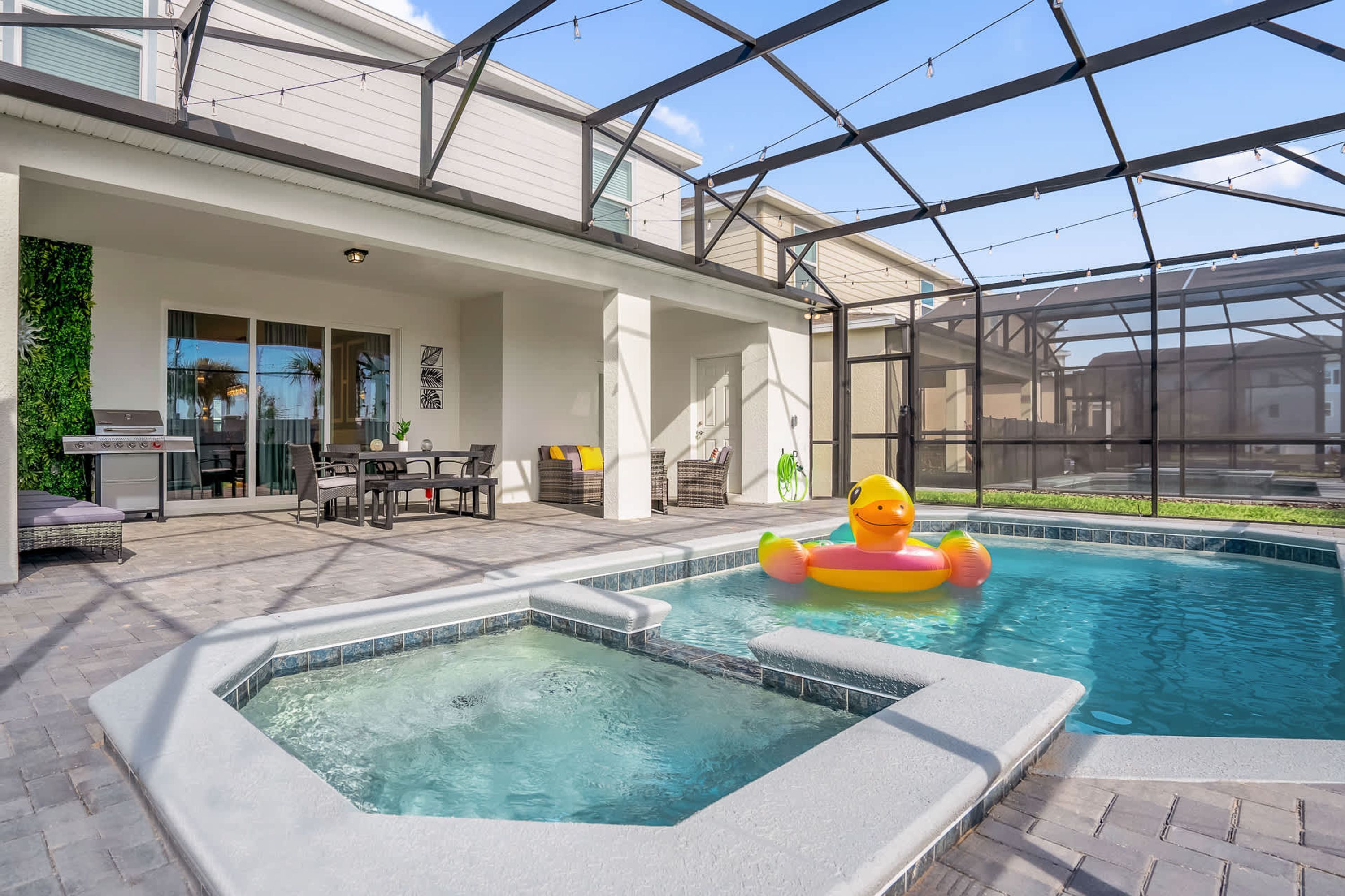 Piscina com hidromassagem, cercada por um alpendre coberto com móveis de exterior e churrasqueira.