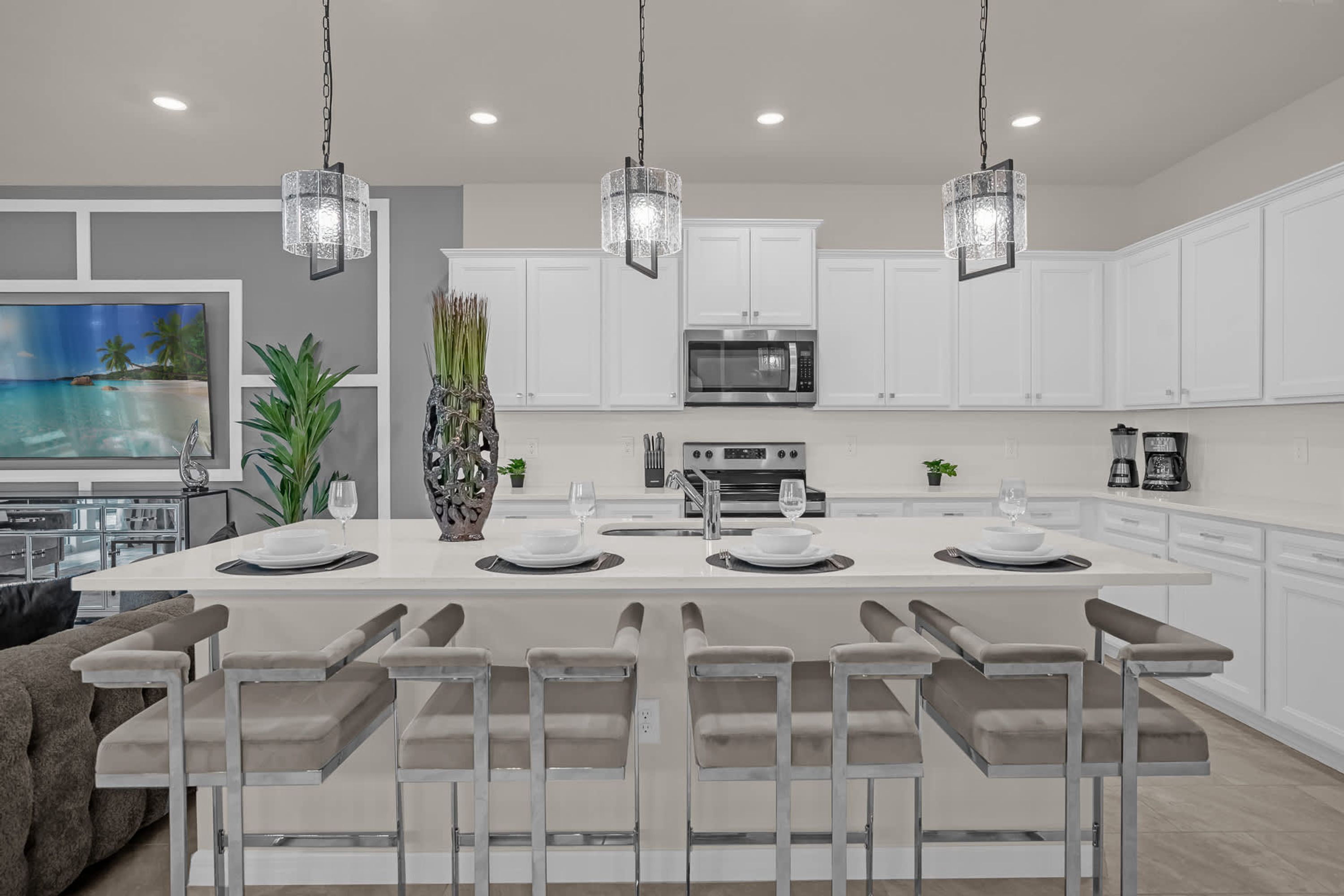 A modern kitchen with white cabinets, a central island with bar seating, and pendant lighting.
