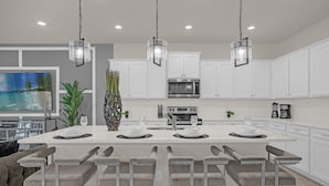 A modern kitchen with white cabinets, a central island with bar seating, and pendant lighting. - Upstay 10br Family Retreat w Pool Hot Tub Games (Clermont)