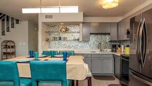 Una cucina moderna con mobili grigi, un frigorifero in acciaio inossidabile e un'area pranzo con sedie color petrolio e un tavolo.