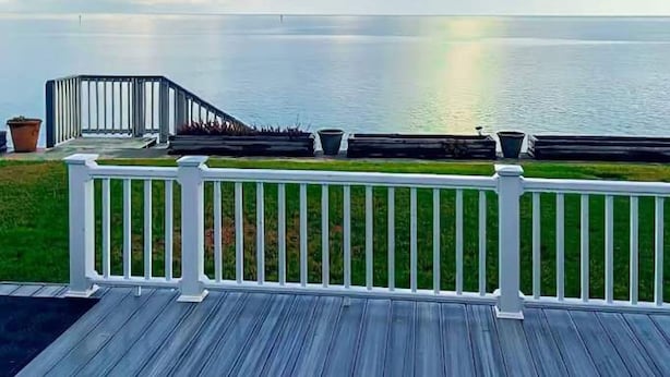 Un pontile di legno con ringhiera bianca, affacciato su un'acqua calma e un cielo sereno con nuvole.
