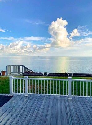 A wooden deck with a white railing, overlooking a calm body of water and a clear sky with clouds. - Bayside Paradise 4BR Home w Patio Games Room (Port Isabel)