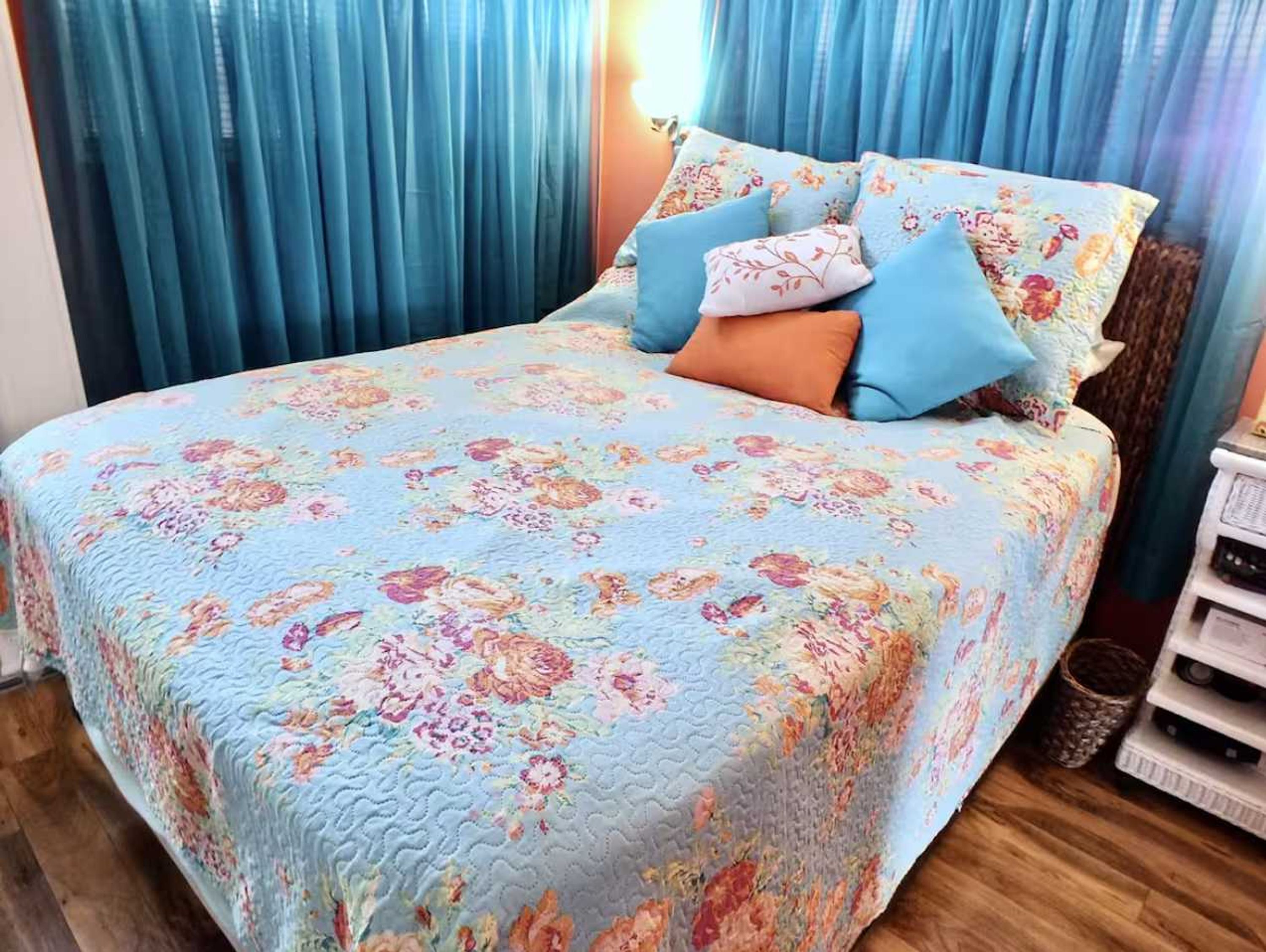 A bed with a floral bedspread, blue curtains, and a wooden floor.