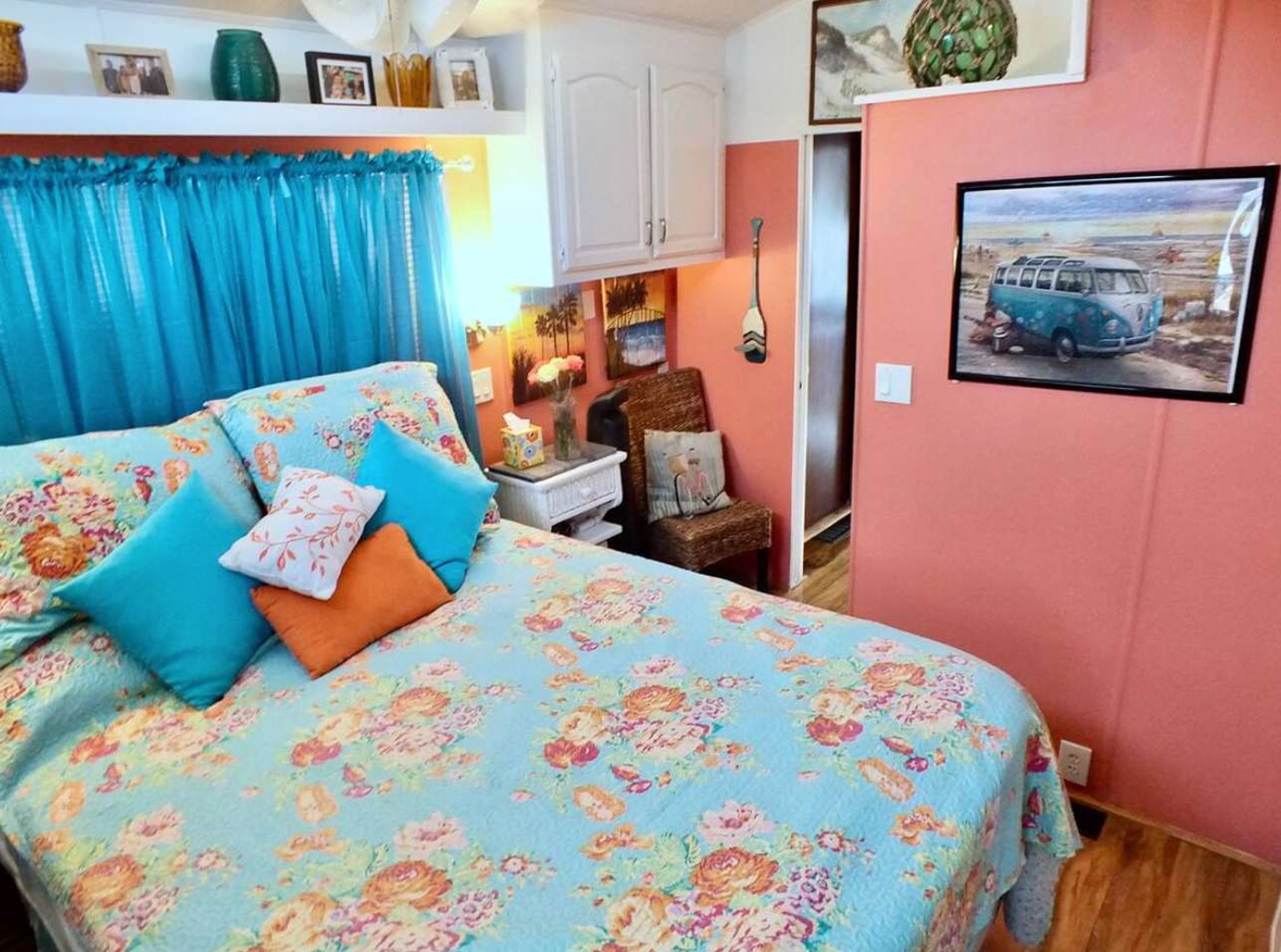 Une chambre à coucher avec une couvre-lit à motifs floraux, un rideau bleu et une affiche représentant une voiture ancienne accrochée au mur.
