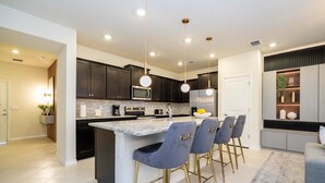A modern kitchen with dark cabinets, a central island with bar stools, and a built-in microwave. - Upstay Family Fun 5BR Retreat w Pool Games Room (Clermont)