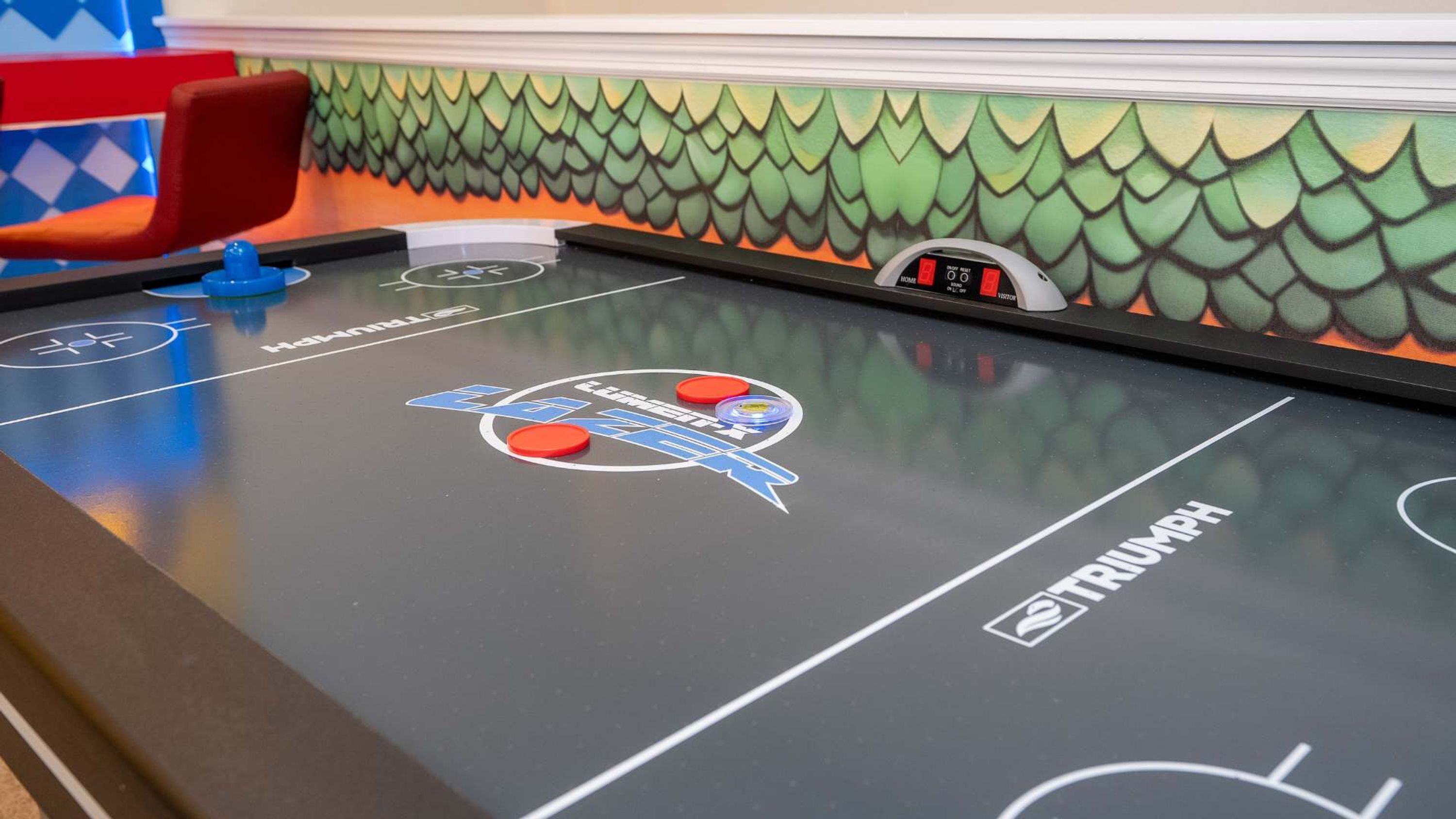 A table hockey game with a fish scale wall design, a red chair, and a digital scoreboard.