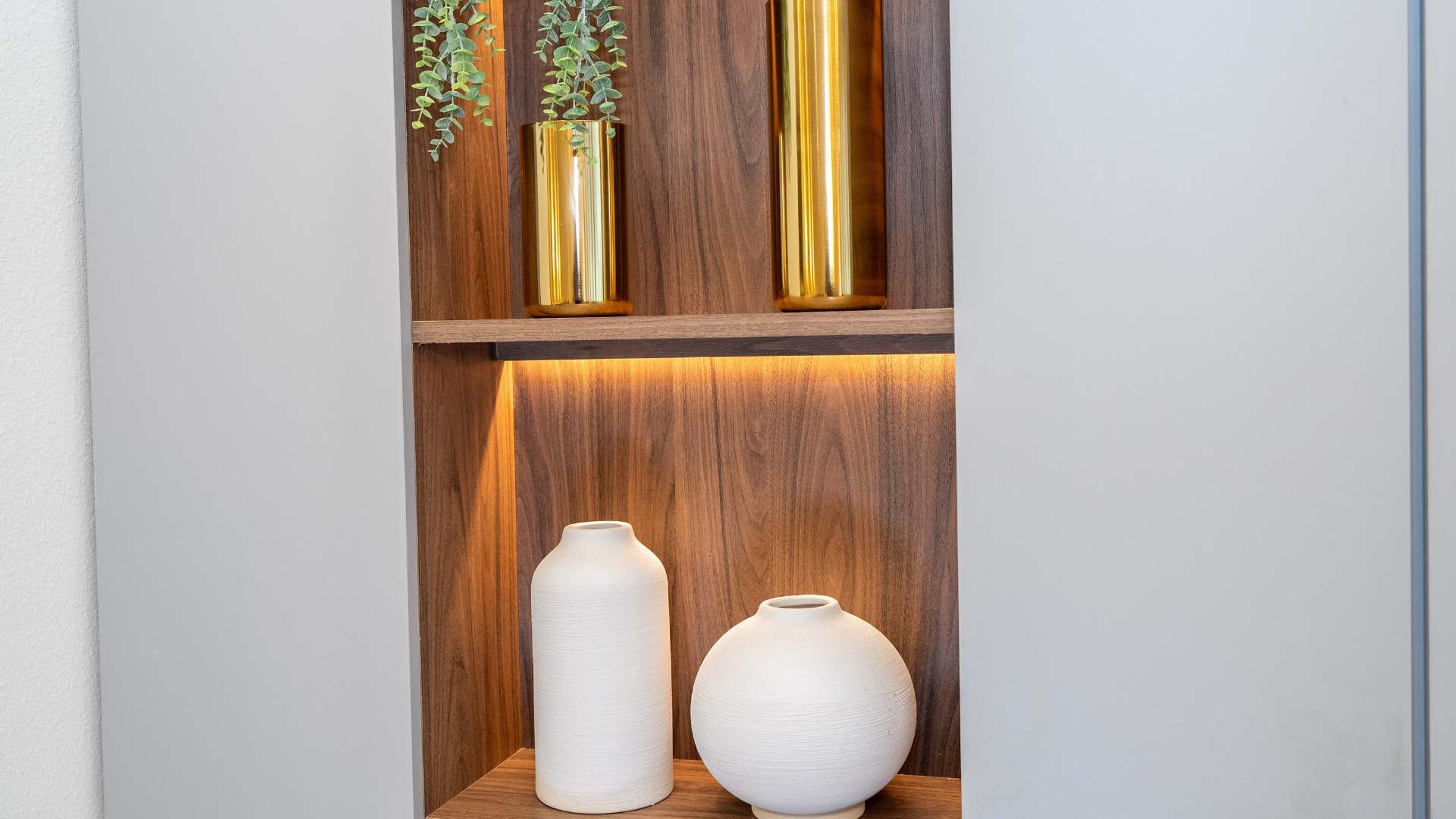 A wooden shelf with three vases, two white and one gold, and a small plant.