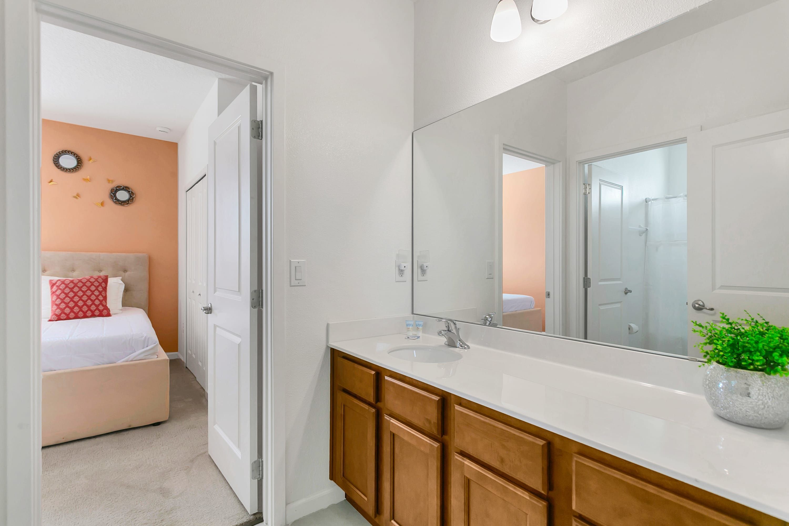 A modern bathroom with a large mirror, wooden cabinets, and a white countertop.