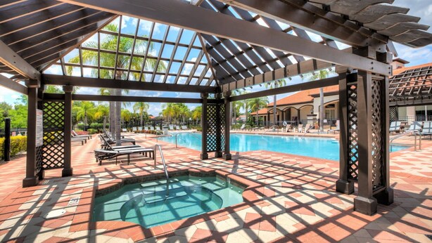 A covered outdoor swimming pool area with a hot tub, lounge chairs, and a pergola structure. - Resort Home w Pool Games BBQ - Near Disney (Kissimmee)