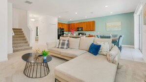 A modern living room with a sectional sofa, a round coffee table, and a dining area with a table and chairs. - Resort Home w Pool Games BBQ - Near Disney (Kissimmee)