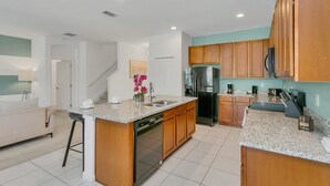A modern kitchen with granite countertops, wooden cabinets, a dishwasher, and a refrigerator. - Resort Home w Pool Games BBQ - Near Disney (Kissimmee)