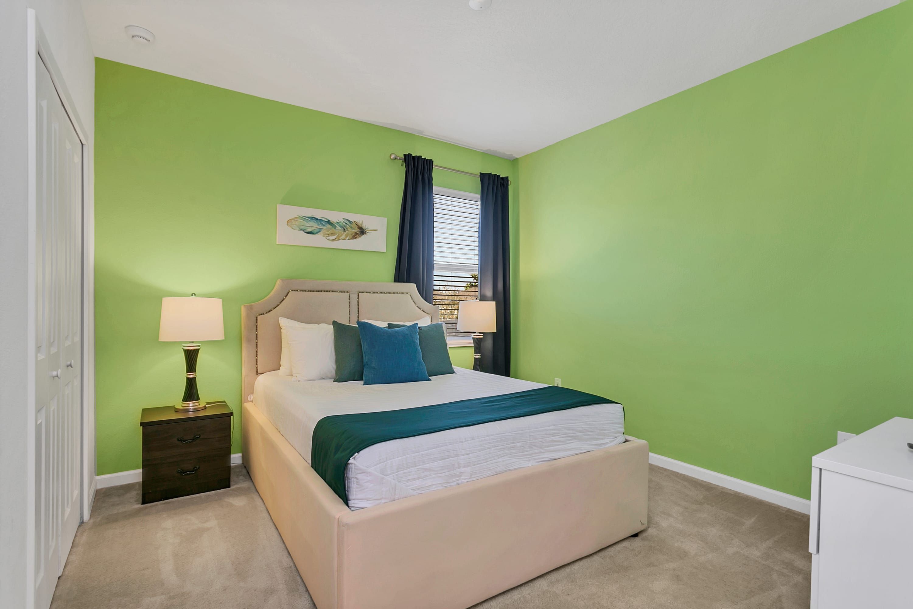Un dormitorio con cama, mesitas de noche, una ventana con cortinas y una pared verde.