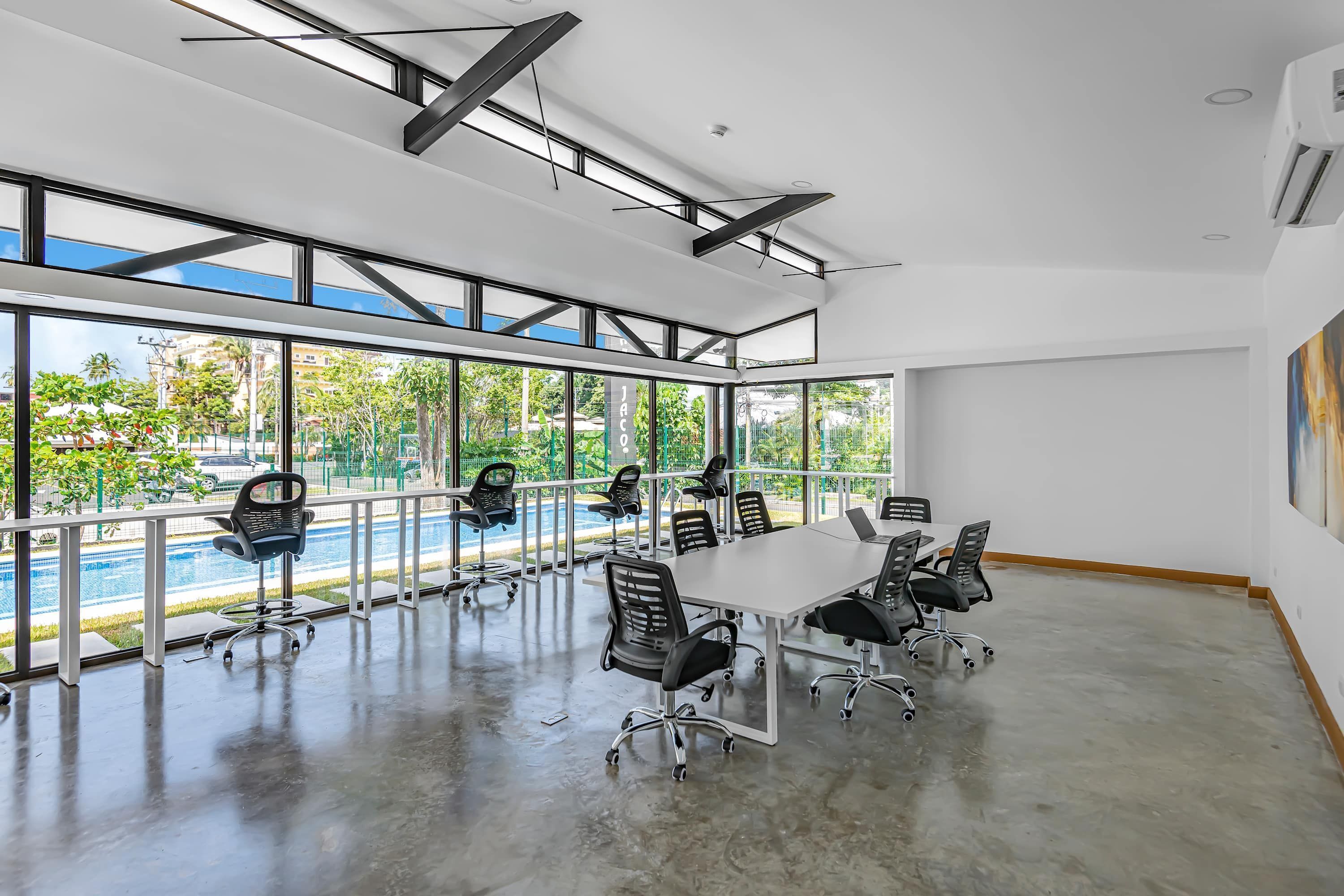 A spacious conference room with a large table and chairs, large windows with a view of a swimming pool and greenery, and a modern ceiling design.