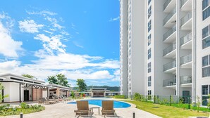 A modern hotel with a swimming pool, lounge chairs, and a tall building in the background. - Contemporary Viva Jaco Residences Suite With Pool (Jacó)