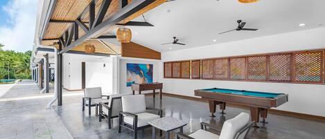 Un espace piscine comprenant une table de billard, des chaises et un grand tableau accroché au mur.