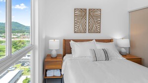 A hotel room with a large window, a neatly made bed, two bedside tables with lamps, and a view of a green landscape. - Contemporary Viva Jaco Residences Suite With Pool (Jacó)