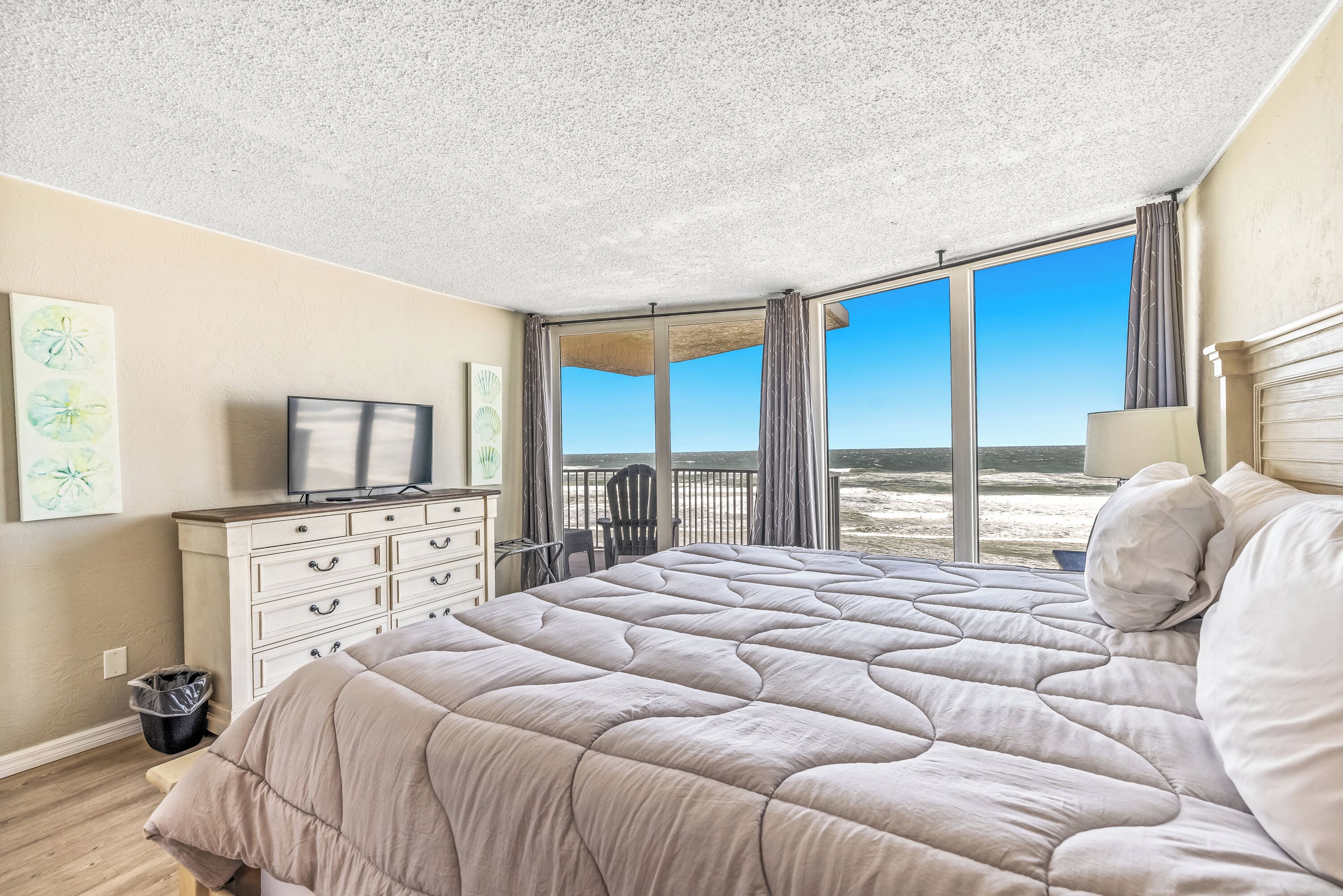 Een slaapkamer met een groot bed, een dressoir, een televisie en uitzicht op het strand.