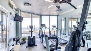 Un gimnasio con cintas de correr, mancuernas y equipo de ejercicio, con vista a una playa.