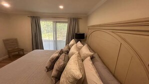 Ein Schlafzimmer mit einem großen Bett, einem Nachttisch, einer Lampe und Blick ins Grüne durch das Fenster.