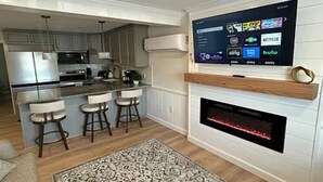 Eine moderne Küche mit einer großen Kochinsel, Barhocker, einem Kamin und einem Wand-Fernseher, der Streaming-Dienste anzeigt.